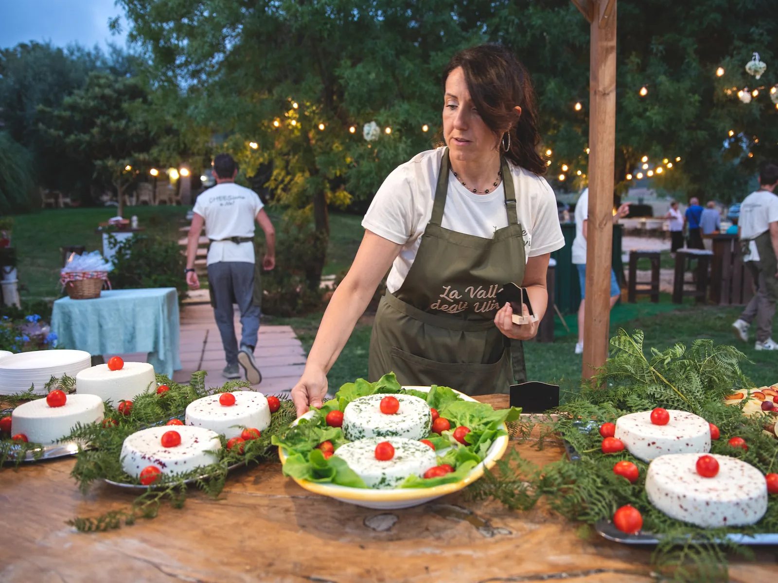 Allestimento del buffet di una festa serale: forme di primo sale decorate con pomodorini, sotto le luci del giardino